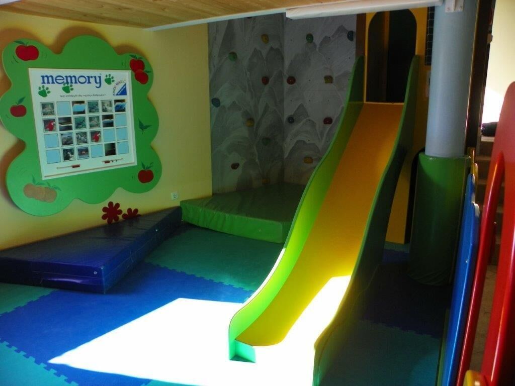 Zona de juegos infantiles con tobogán, piso acolchado y un cartel con recuerdos.