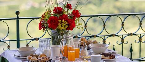 A table set for breakfast with various dishes, a pitcher of orange juice, and a vase of red flowers.
