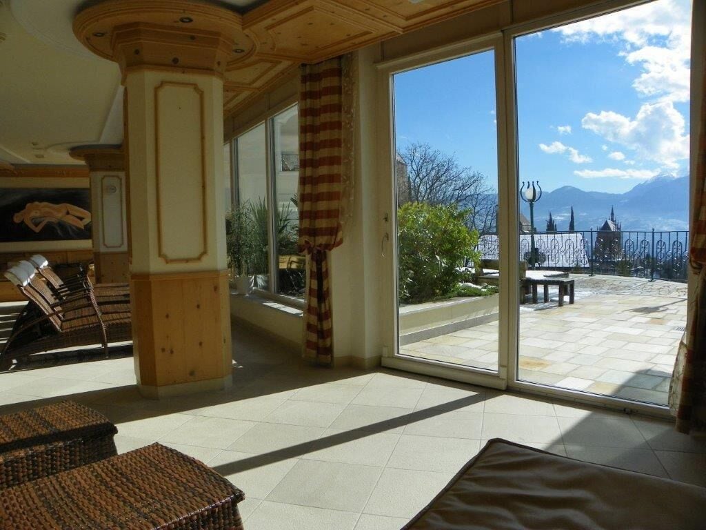 Um quarto amplo com uma grande porta de correr de vidro que dá para um pátio externo. No interior, há móveis de vime e teto de madeira.