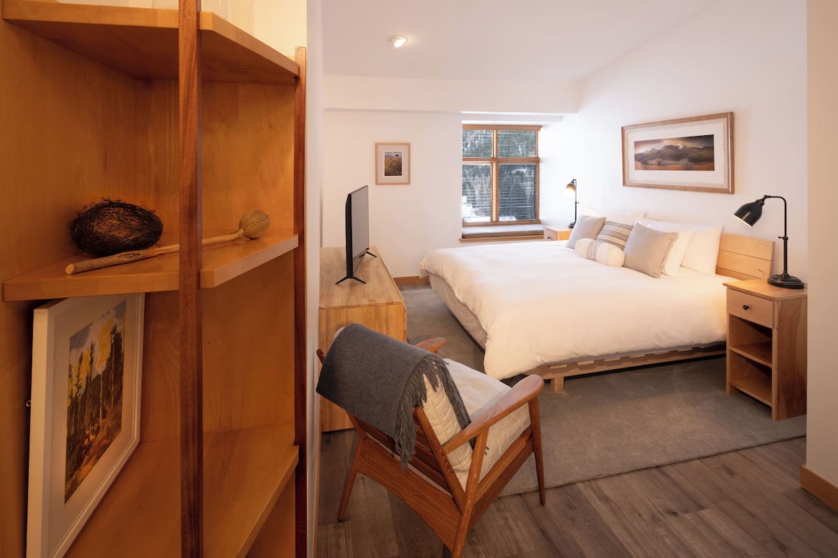 A bedroom with a bed, wooden furniture, a window, and a painting on the wall.