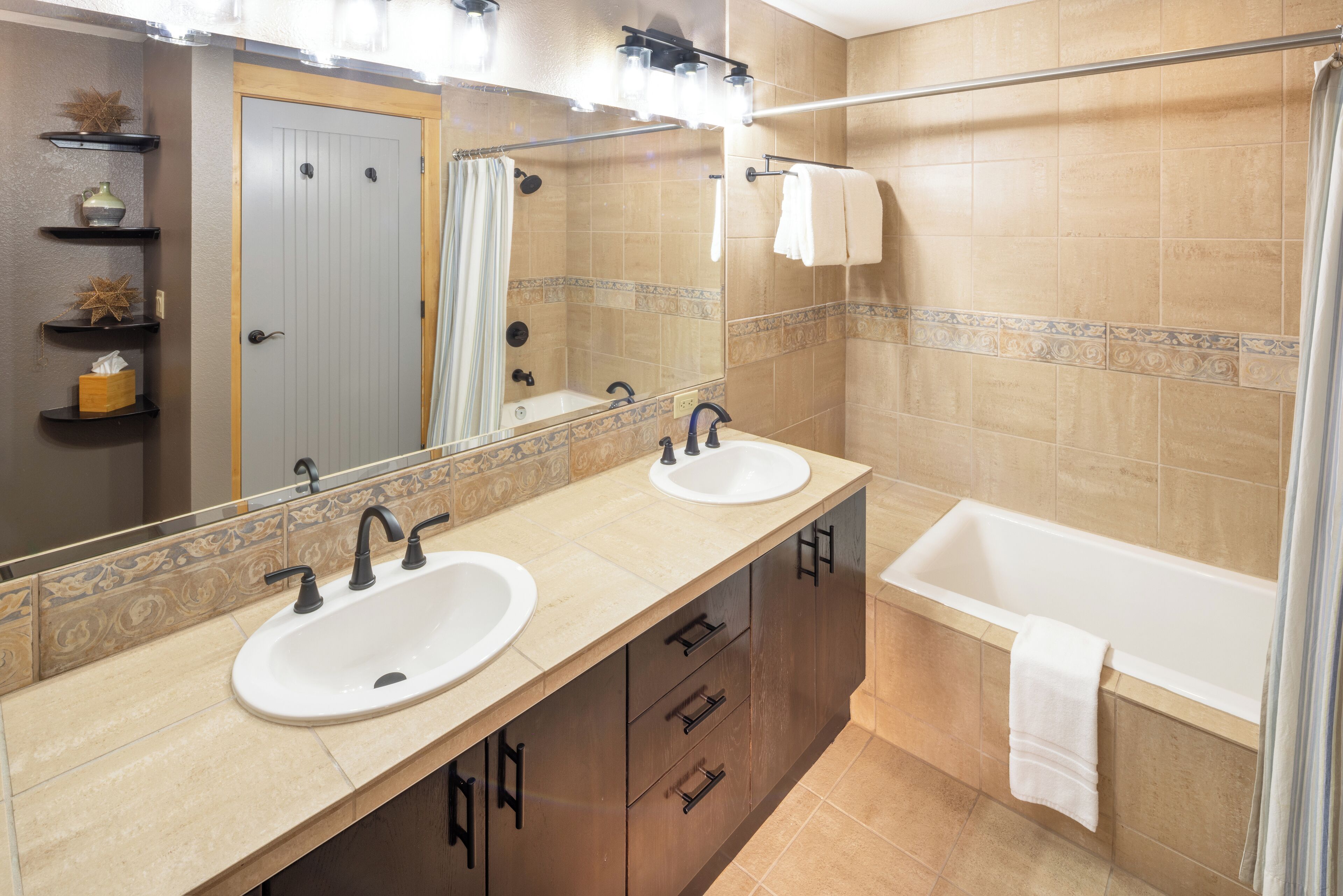 Une salle de bain avec deux lavabos, une baignoire et une douche. On y trouve des étagères avec des articles de toilette et un miroir au-dessus des lavabos.