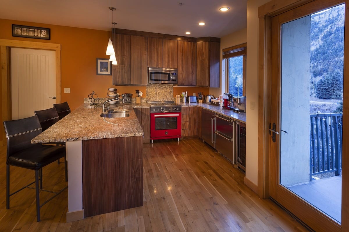 A kitchen with wooden cabinets, a granite countertop, a red oven, and a large sliding glass door to a balcony.