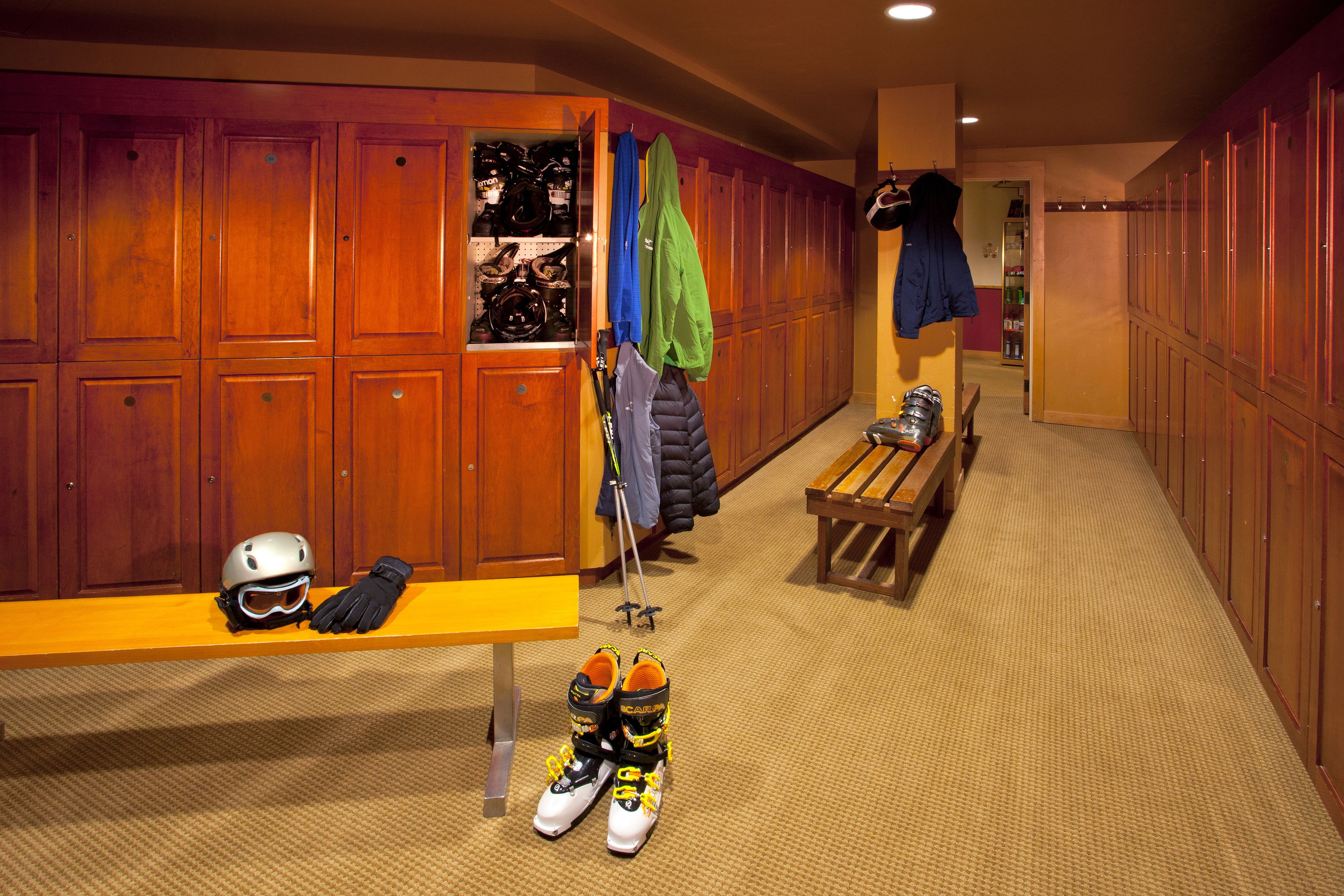 A locker room with wooden lockers, a bench, and a table with ski gear.