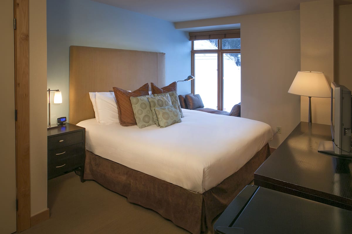 A hotel room with a large bed, a nightstand with a lamp, a dresser, and a window with a view.