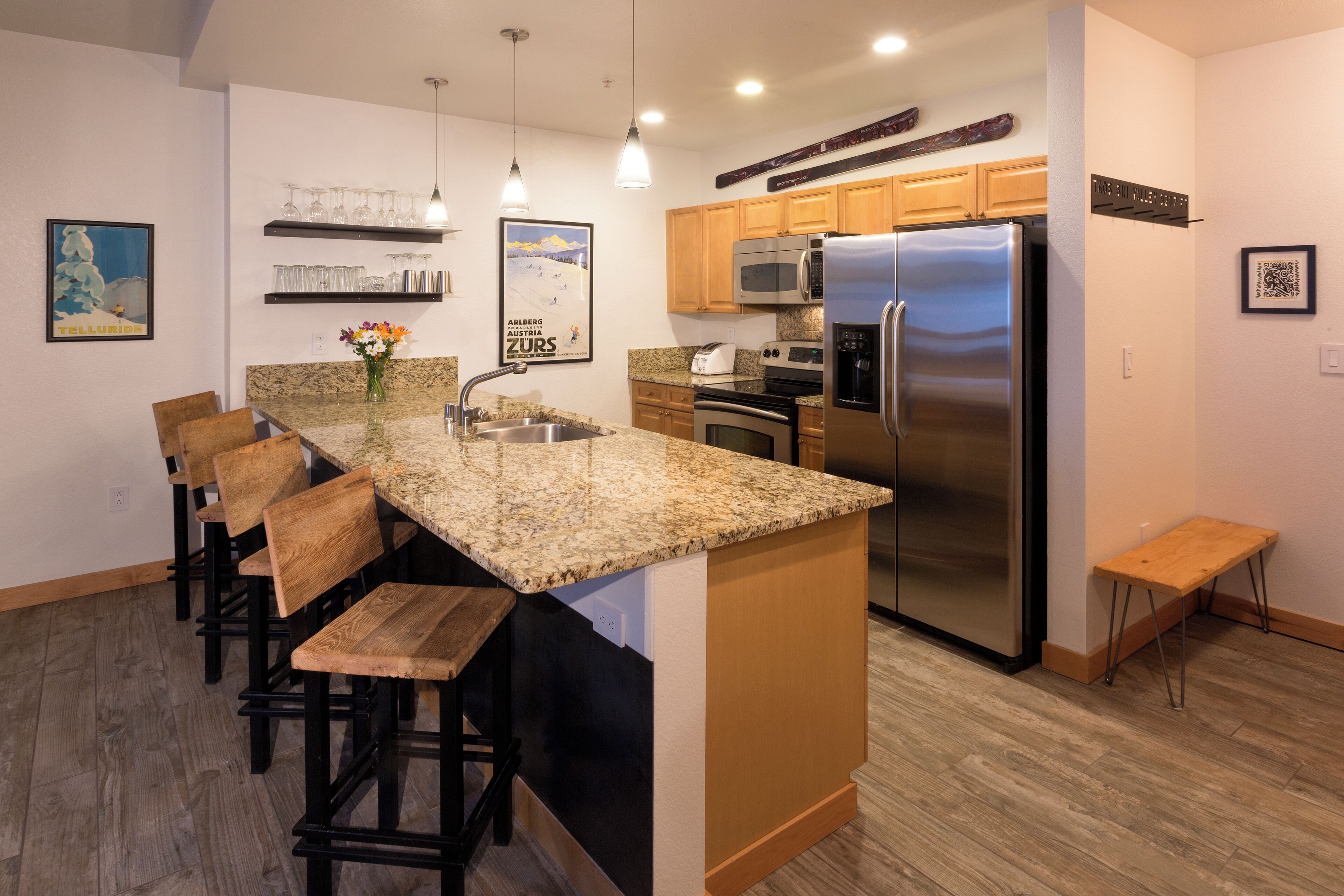 A modern kitchen with granite countertops, stainless steel appliances, wooden bar stools, and a built-in island.