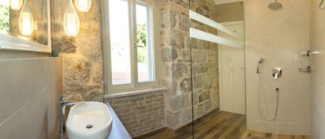 A bathroom with a stone wall, a sink, a shower, and a window with natural light.