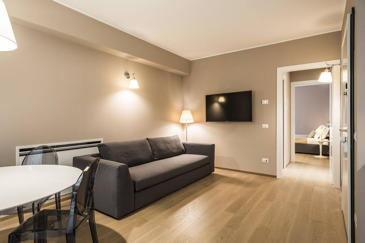 A modern living room with a grey sofa, a round dining table, and a TV mounted on the wall.