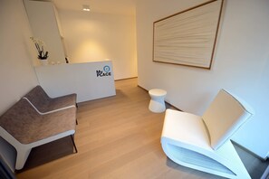 A modern reception area with a reception desk labeled "My Place," a brown and white chair, a white chair, and a small round table. - MYSWEETPLACE - Corso Como Apartments (Milan)