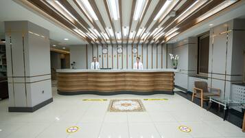A reception area with a wooden reception desk, two receptionists, and a decorative rug.