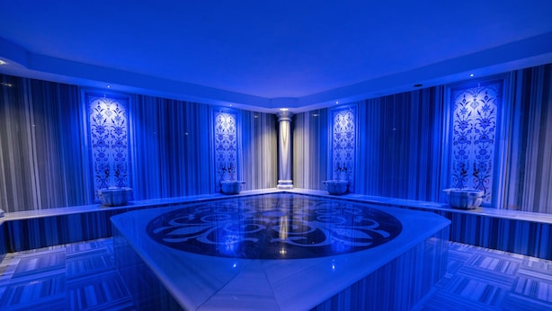 Een luxe kamer met een grote centrale tafel, versierde wandpanelen en een spiegelende vloer.