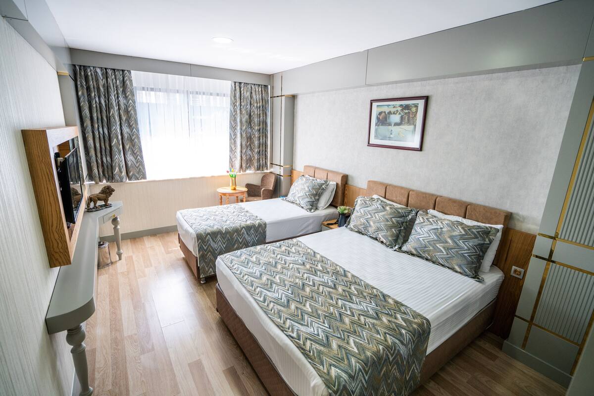 Habitación de hotel con dos camas, un escritorio y una ventana con cortinas.