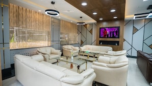 Een moderne woonkamer met een zithoek, een glazen salontafel en een flatscreen televisie aan de muur.
