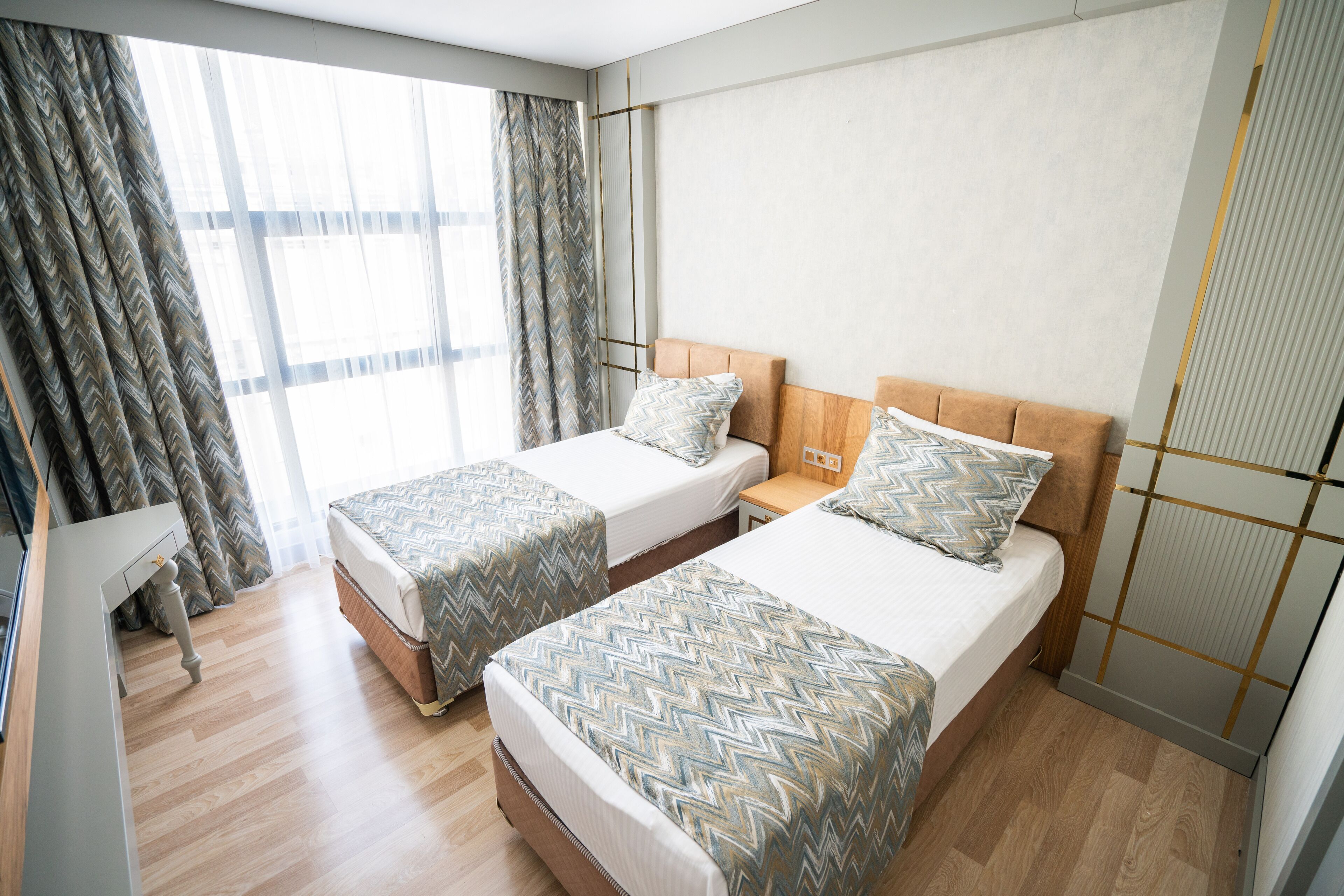 A hotel room with two beds, a desk, and a large window with curtains.