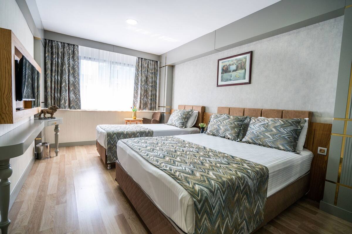 Habitación de hotel con dos camas, un escritorio, una silla, un espejo y una ventana con cortinas.