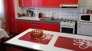 A kitchen with red cabinets, a white countertop, a stove, a sink, and a microwave. - Large Apartment in the heart of Slovácko (Kunovice)