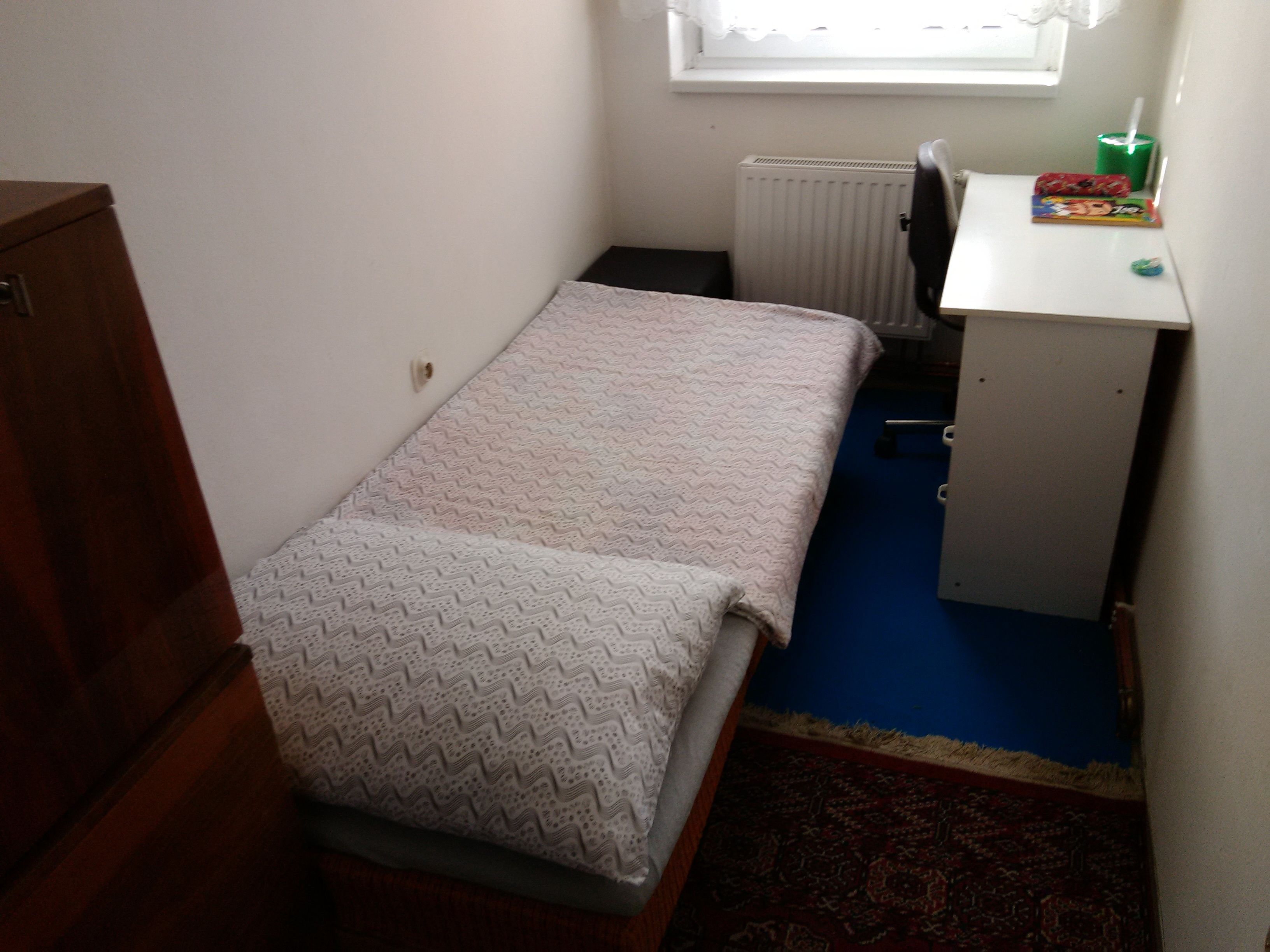 A small, single-bed room with a desk and radiator.