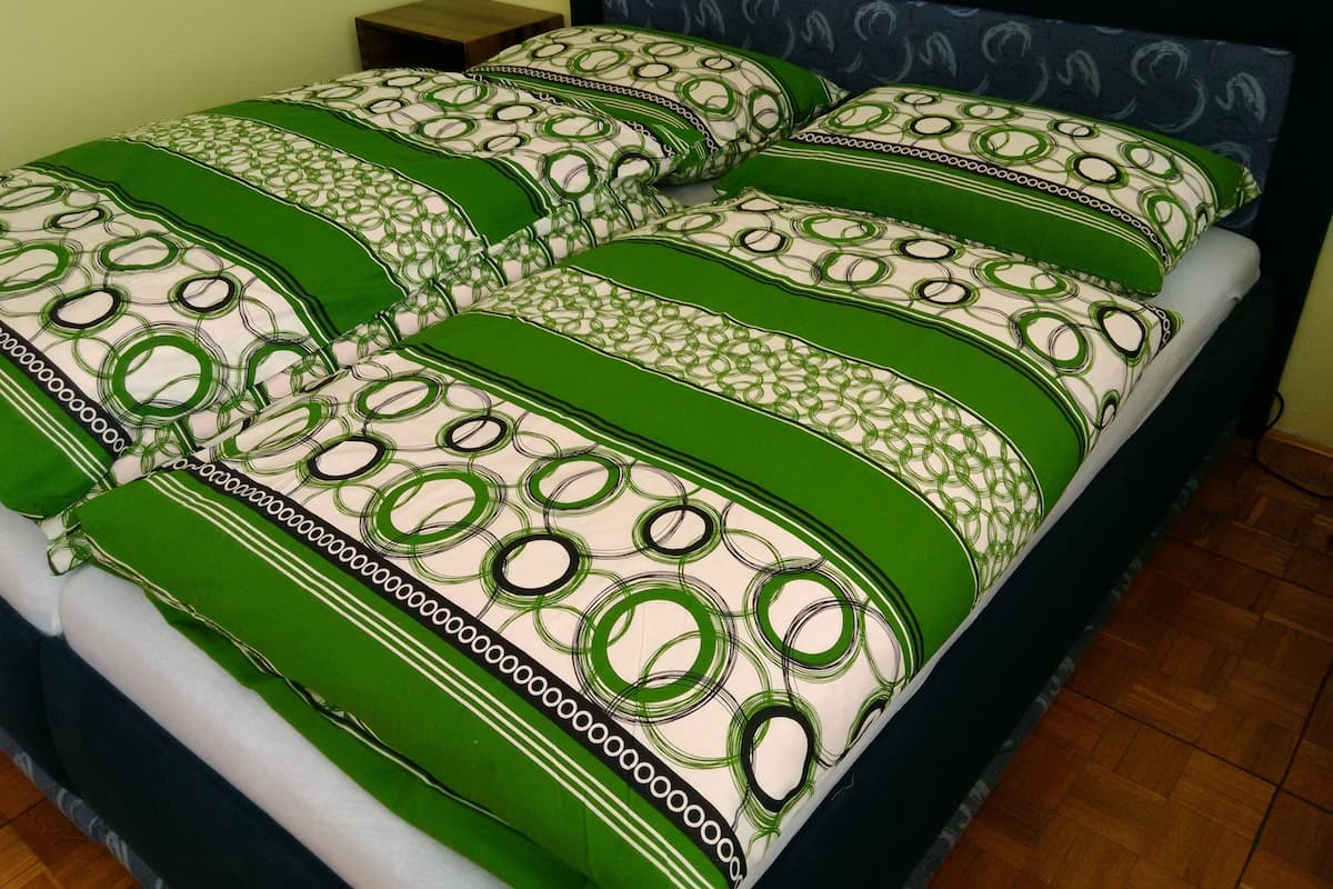 A bed with green and white patterned bedding, a wooden nightstand, and a dark headboard.