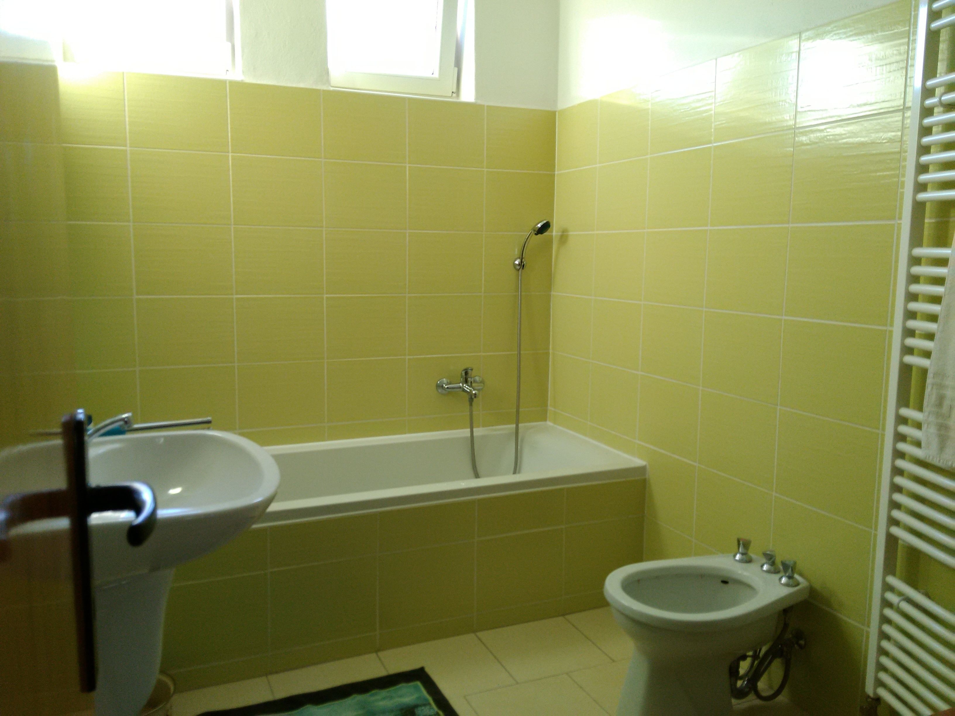 Un baño con baldosas amarillas, una bañera, un bidé y un lavamanos.