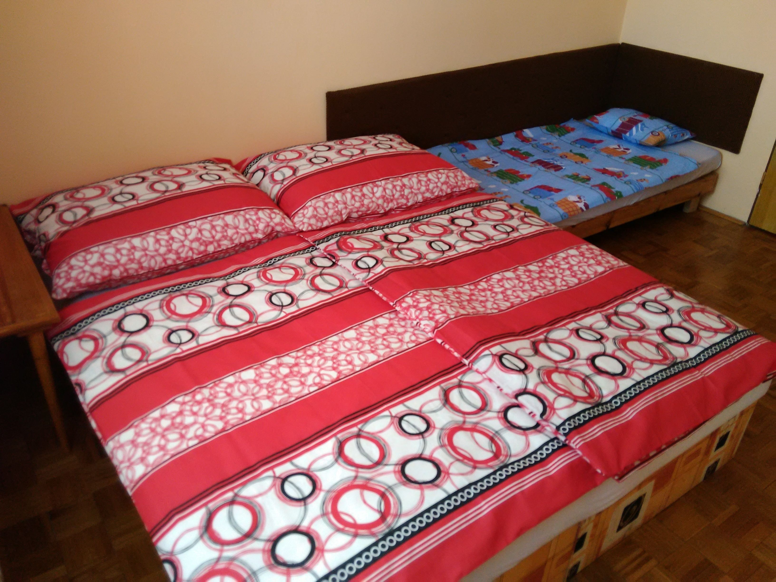 Una habitación con dos camas, una con ropa de cama blanca y roja estampada y la otra con ropa de cama azul con personajes de caricaturas.