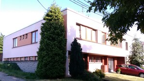 A modern two-story house with a large tree in the front yard, a red car parked nearby, and a clear sky. - Large Apartment in the heart of Slovácko (Kunovice)