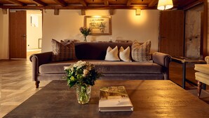 A cozy living room with a wooden ceiling, a brown sofa with patterned cushions, a vase with flowers, and a book on a wooden coffee table. - Chateau Salavaux (Vully-les-Lacs)