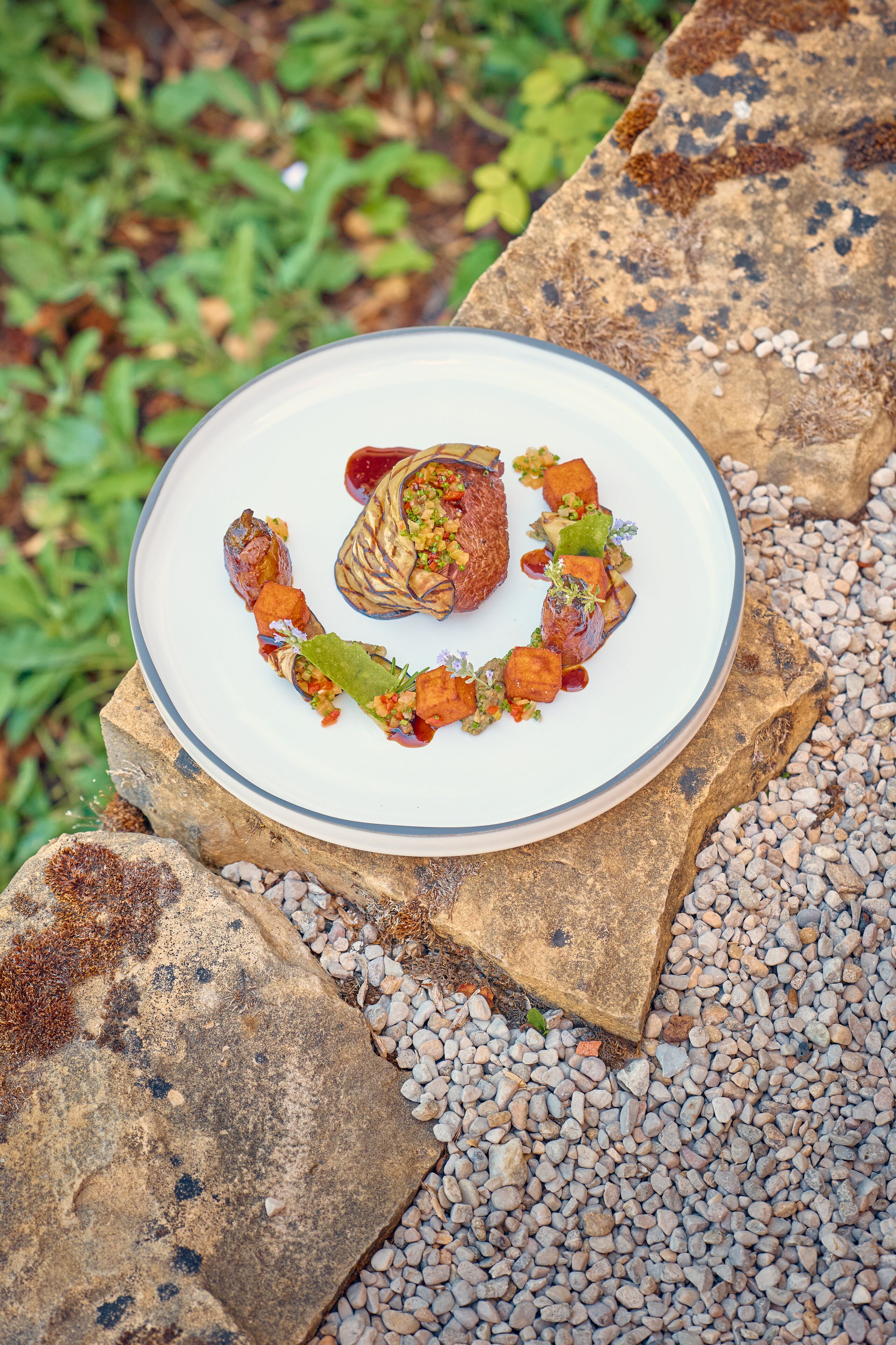 A plate of food on a stone slab with pebbles around it.