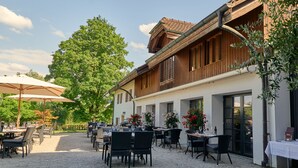 An outdoor dining area with tables and chairs, surrounded by a building with wooden shutters and a tiled roof. - Chateau Salavaux (Vully-les-Lacs)