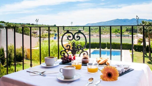 A breakfast table with coffee, juice, pastries, and a flower on a balcony overlooking a pool and mountains. - Hotel La Cava (Cabanes)