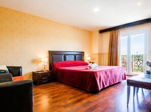 A hotel room with a large bed, wooden floor, a small desk, and a balcony with a railing. - Hotel La Cava (Cabanes)