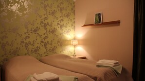 A room with two beds, a nightstand with a lamp, a shelf with a picture, and a window with curtains. - Hotel Vuollerim (Vuollerim)