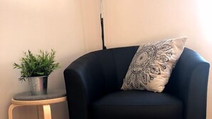 A black armchair with a patterned pillow, a small wooden side table with a potted plant, and a pink rug on a wooden floor. - Hotel Vuollerim (Vuollerim)