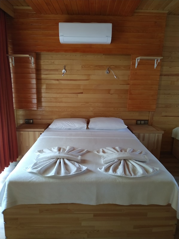 A wooden room with a bed, white bedding, and an air conditioning unit. - Olympos Yavuz Hotel (Kemer)