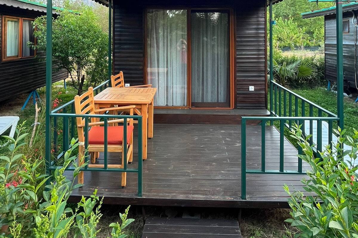 Eine Holzhütte mit überdachter Veranda, einem Esstisch mit Stühlen und einem kleinen Garten.