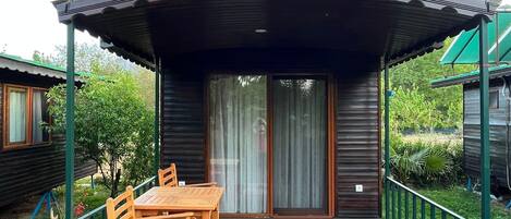 A wooden cabin with a covered porch, a dining table with chairs, and a small garden area.