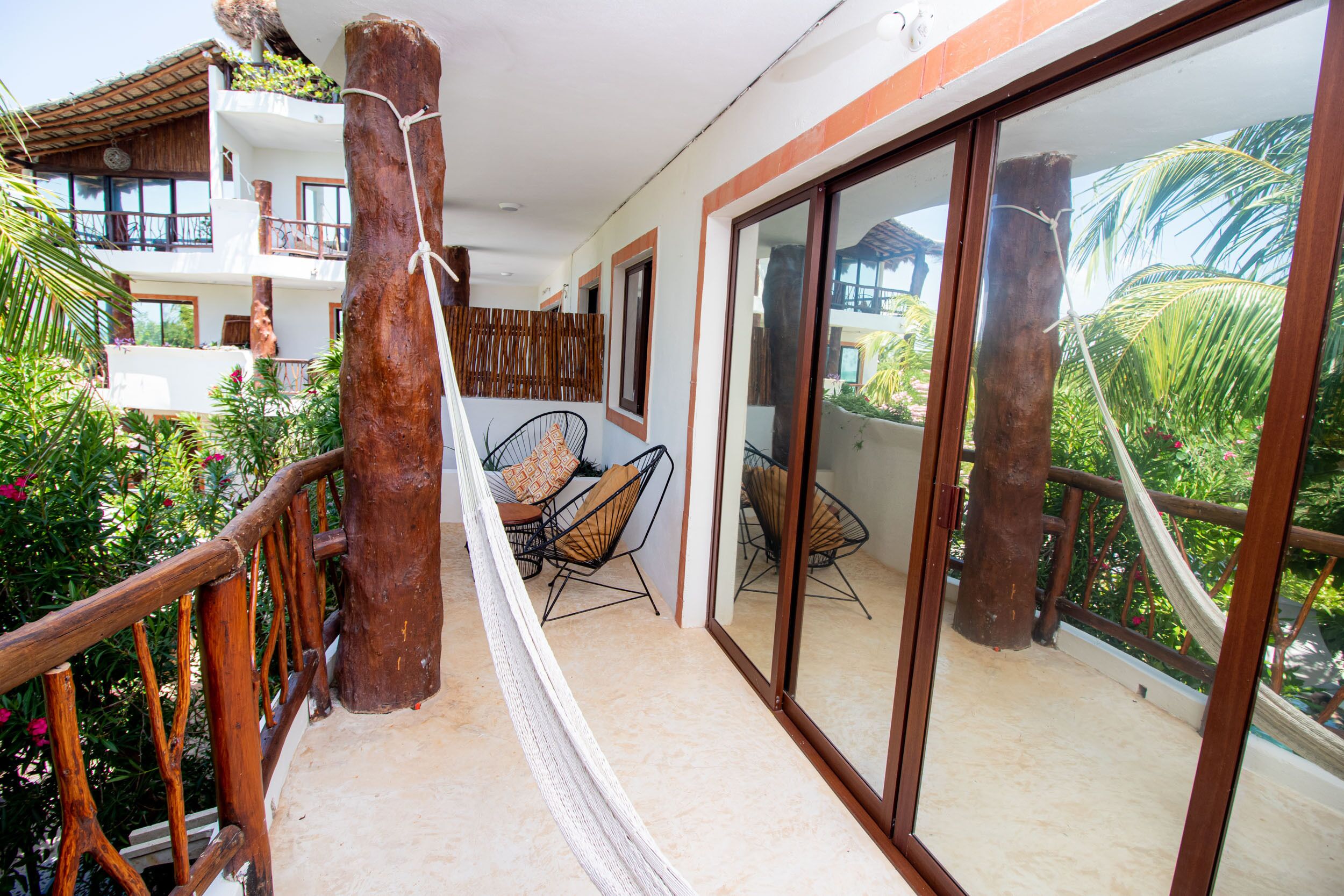 A balcony with a hammock, wicker chairs, and a view of a neighboring building.
