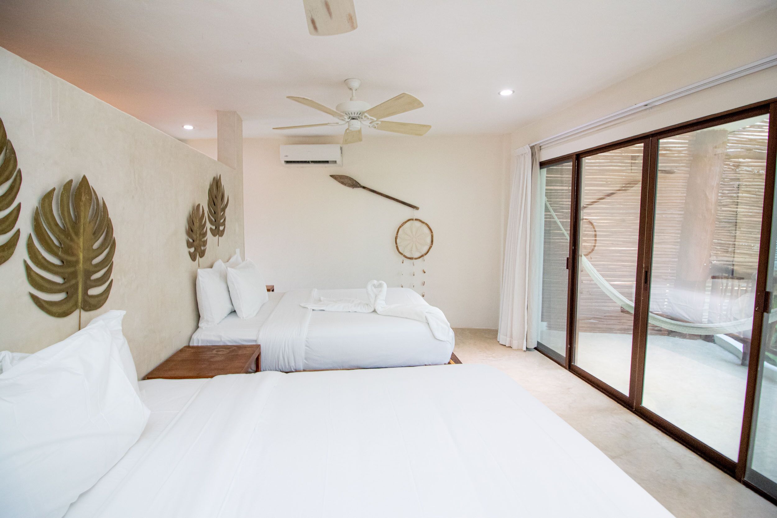 A bedroom with two beds, a ceiling fan, and a view of a wooden deck through large sliding glass doors.