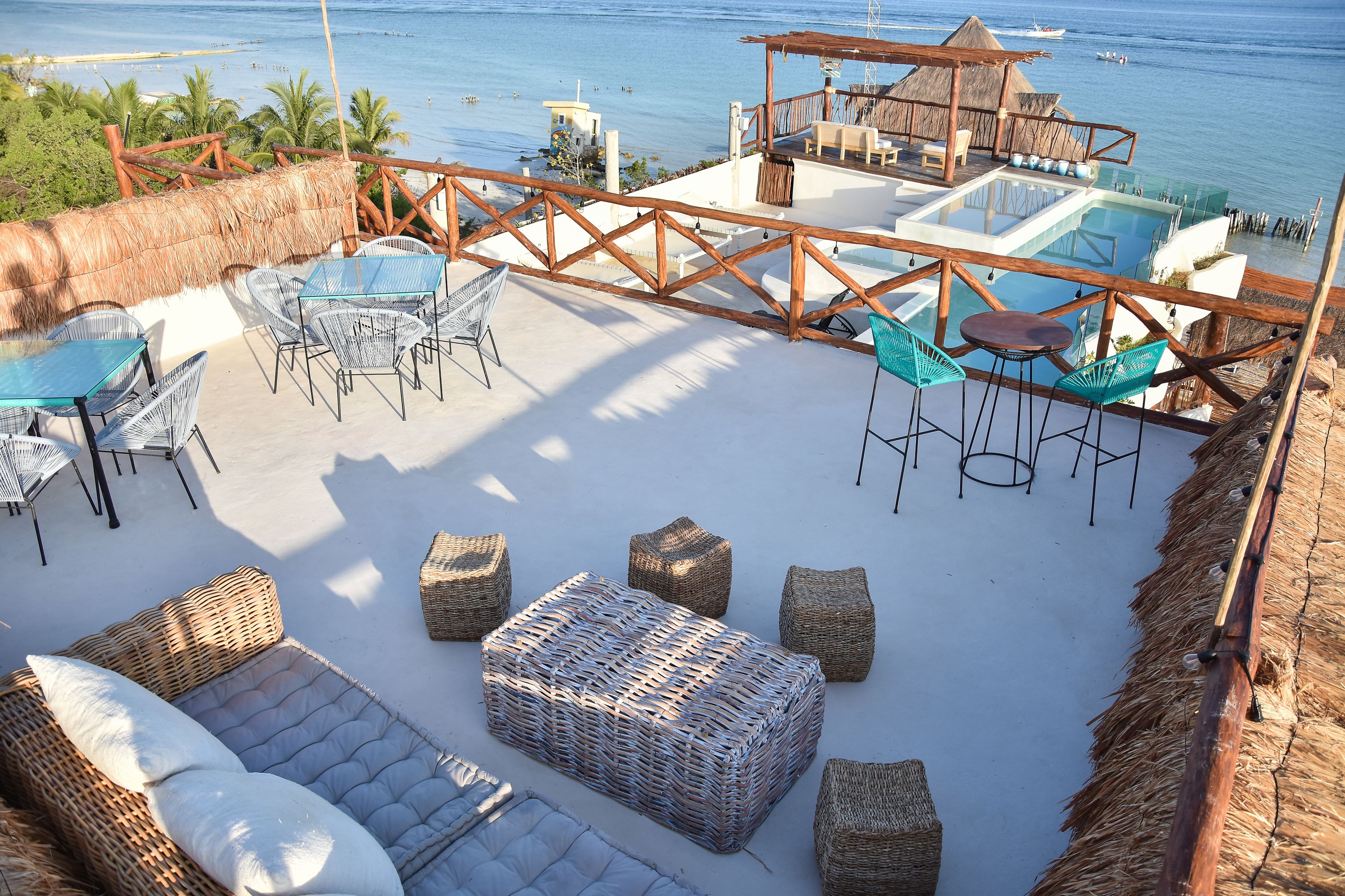Un salon de plage doté d’une piscine à débordement en verre, de meubles en osier et offrant une vue sur l’océan.