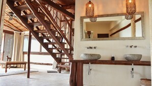 Una escalera de madera de diseño rústico, un espejo grande sobre un lavamanos doble, y una lámpara colgante.