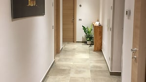 A hallway with a tiled floor, a wooden door, a wall-mounted light fixture, and a framed picture on the wall. - Alludo B&B (Agrigento)