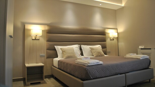 A modern hotel room with a large bed, bedside lamps, a nightstand, and an air conditioning unit. - Alludo B&B (Agrigento)