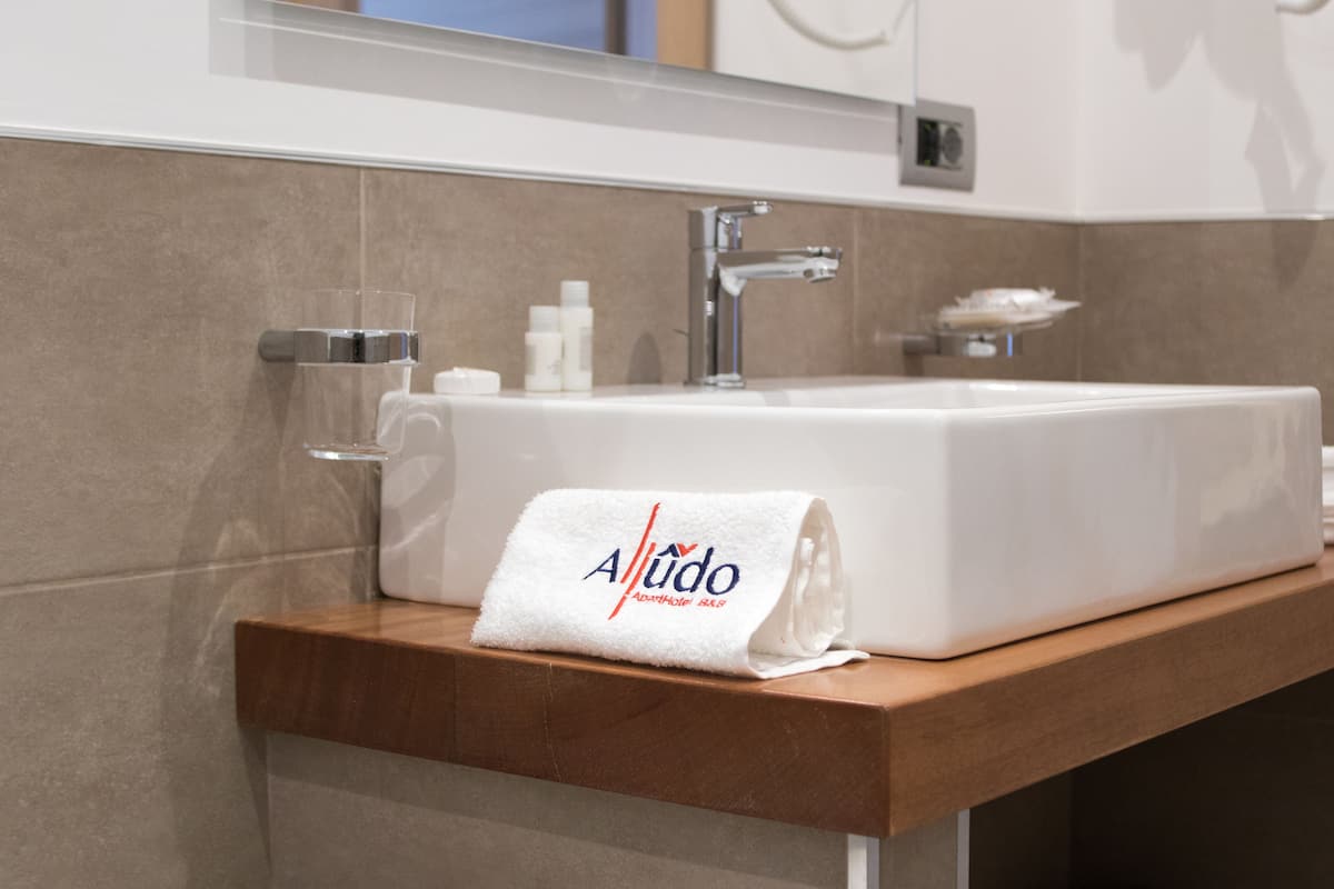 Un baño con lavamanos blanco, una toalla con el logo "Aludo" y encimera de madera.