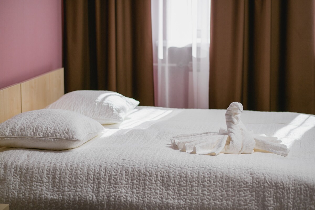 Un lit bien fait, avec une couette blanche à texture et des oreillers, une serviette pliée et une tête de lit en bois.