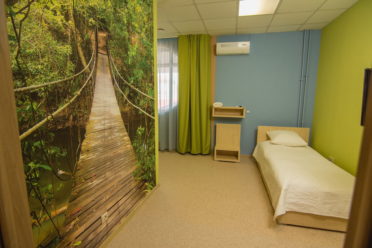 Une chambre avec un lit, une petite table de chevet, un climatiseur fixé au mur et un rideau.