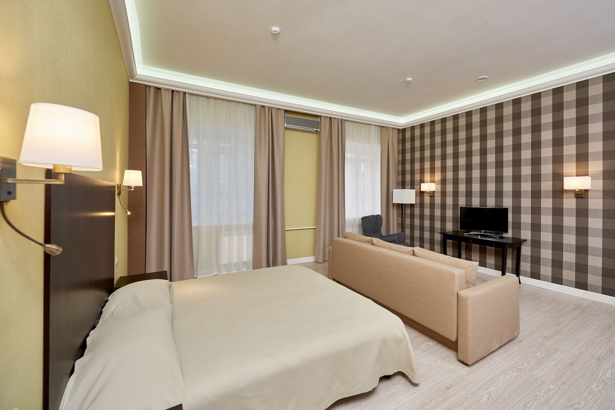 Une chambre d’hôtel avec un grand lit, un canapé, un téléviseur posé sur un meuble et un mur à carreaux.
