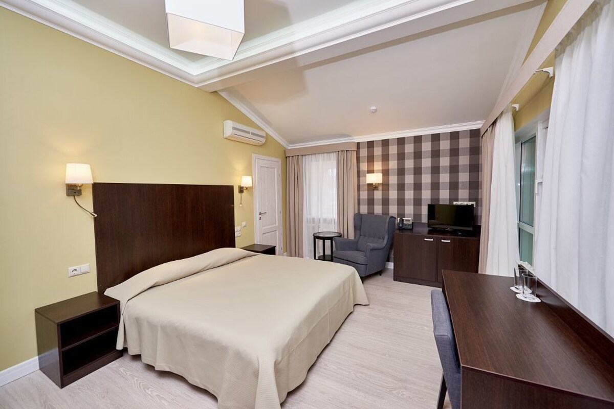 Une chambre d’hôtel avec un grand lit, un bureau, une chaise, une télévision et une fenêtre avec des rideaux.