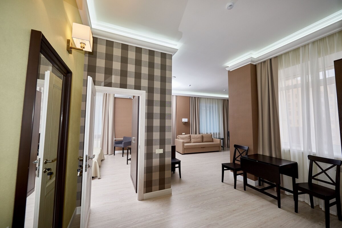 Une chambre d’hôtel avec un mur à carreaux, un canapé, une table à manger avec des chaises et une vue sur la ville grâce à de grandes fenêtres.