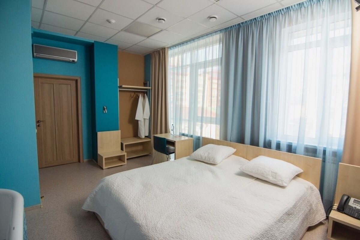 Une chambre d’hôtel comprenant un lit, un bureau, une chaise, une armoire et une fenêtre avec des rideaux.