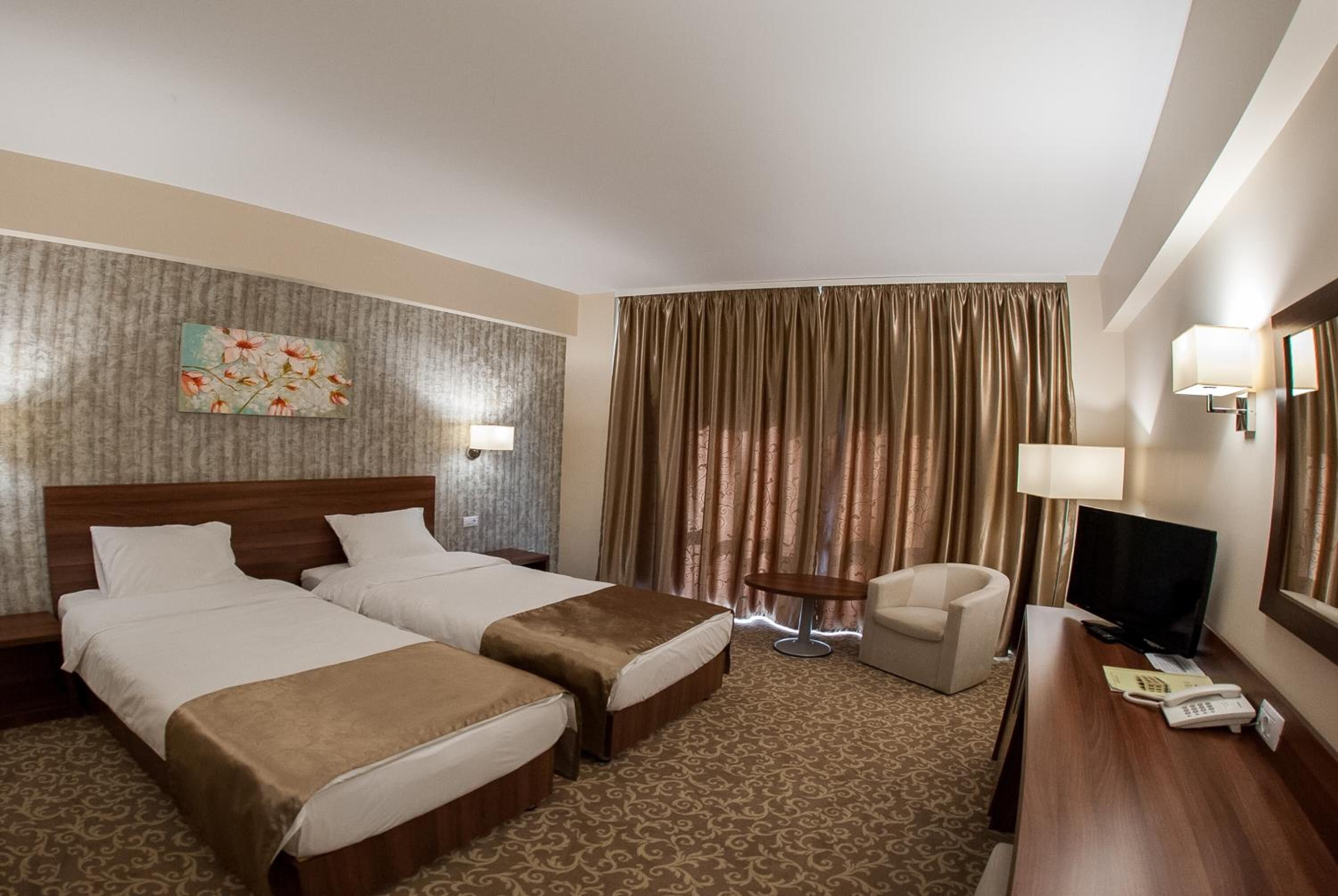 A hotel room with two beds, a desk, a chair, a television, and a window with curtains.