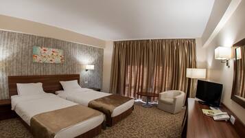 A hotel room with two beds, a desk, a chair, a television, and a window with curtains.