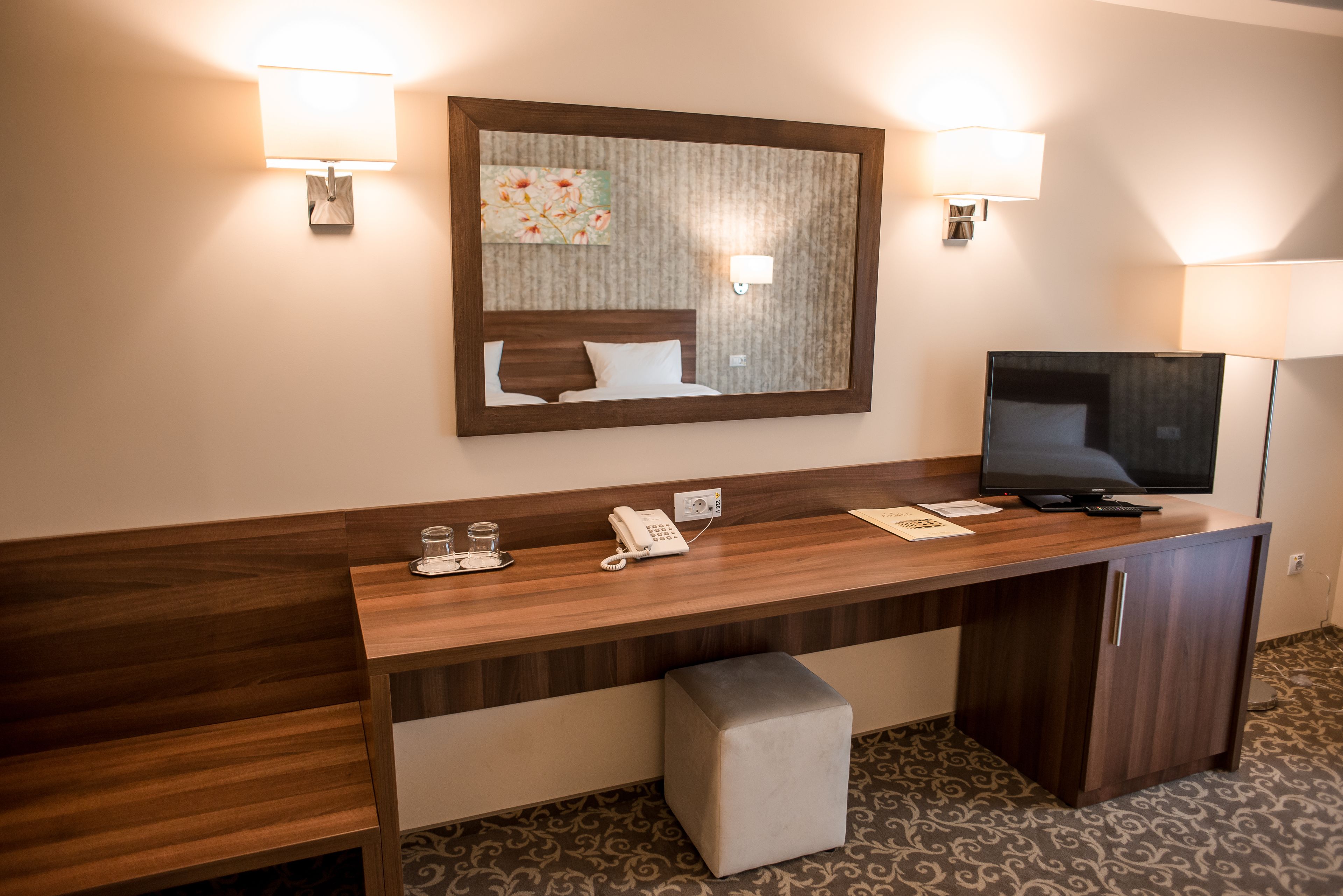 A hotel reception desk with a flat-screen TV, a telephone, and a small table with a glass and a cup.
